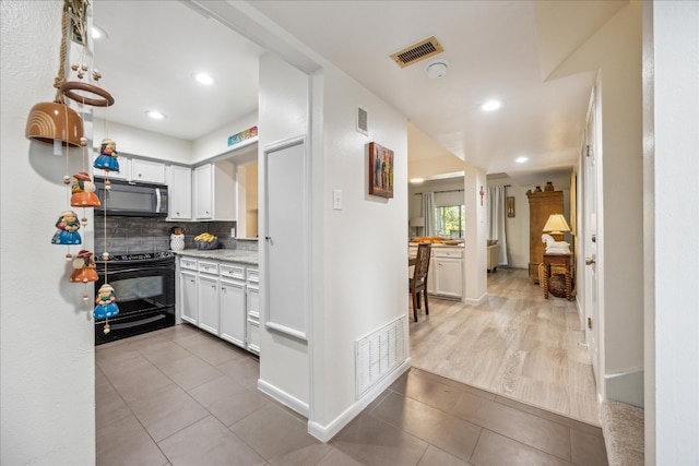 kitchen featuring backsplash, tile patterned floors, black electric range oven, and white cabinets