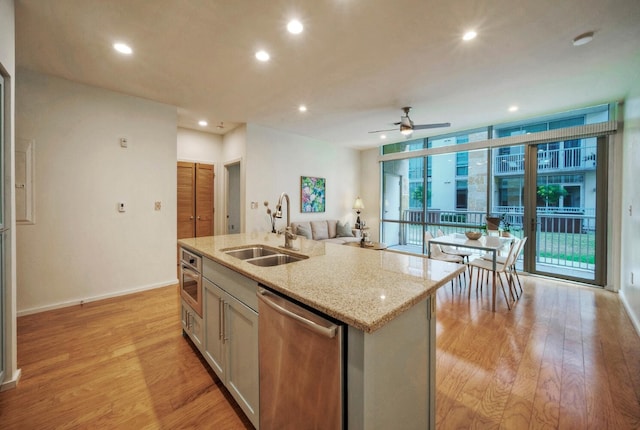 kitchen with ceiling fan, sink, stainless steel dishwasher, a center island with sink, and light wood-type flooring