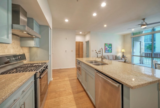 kitchen featuring light stone counters, sink, wall chimney exhaust hood, stainless steel appliances, and light wood-type flooring