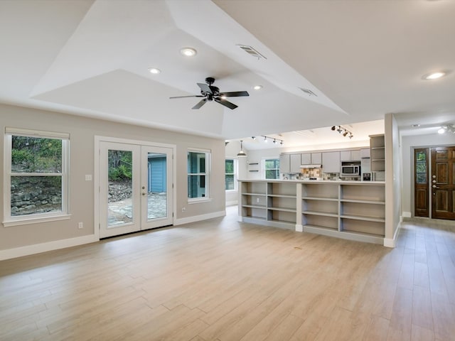 unfurnished living room featuring a raised ceiling, ceiling fan, french doors, and light wood-type flooring