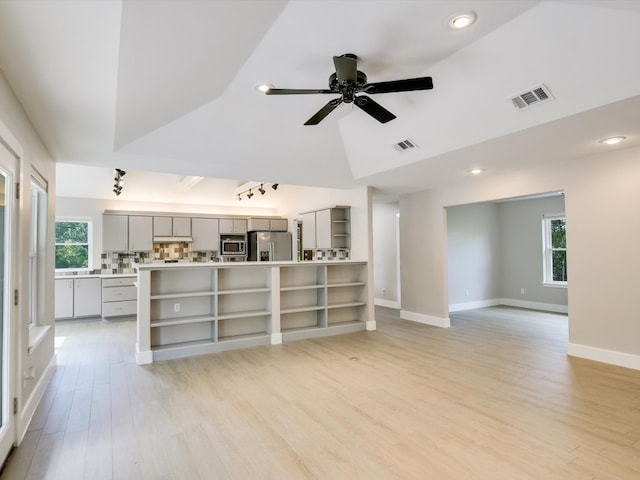 unfurnished living room with a raised ceiling, ceiling fan, light hardwood / wood-style floors, and vaulted ceiling