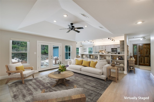 living room with hardwood / wood-style floors, a raised ceiling, a wealth of natural light, and french doors