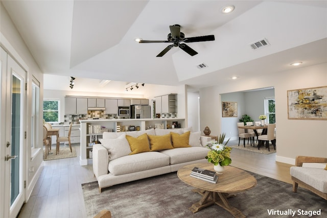 living room with a tray ceiling, ceiling fan, vaulted ceiling, and light wood-type flooring