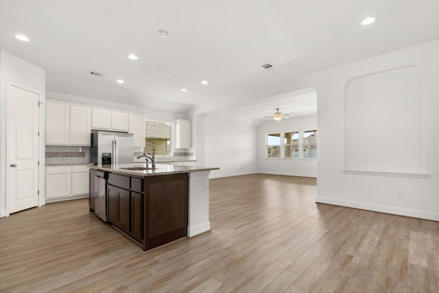 kitchen with ceiling fan, stainless steel appliances, a center island with sink, white cabinets, and light wood-type flooring