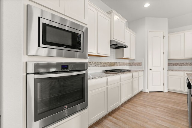 kitchen with white cabinetry, stainless steel appliances, range hood, light hardwood / wood-style floors, and decorative backsplash