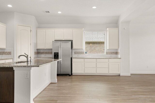 kitchen with visible vents, a sink, light stone counters, stainless steel fridge, and white cabinets