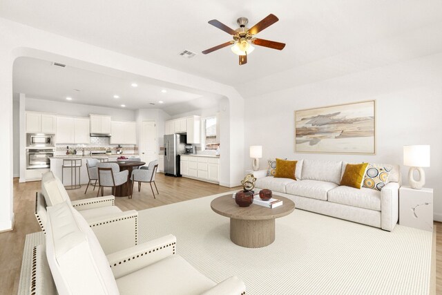 living room featuring light wood-style flooring, a ceiling fan, and visible vents