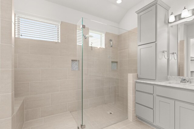 full bath featuring a tile shower, vanity, and vaulted ceiling