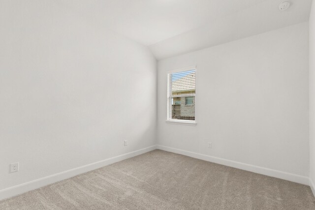 spare room featuring carpet flooring, baseboards, and vaulted ceiling