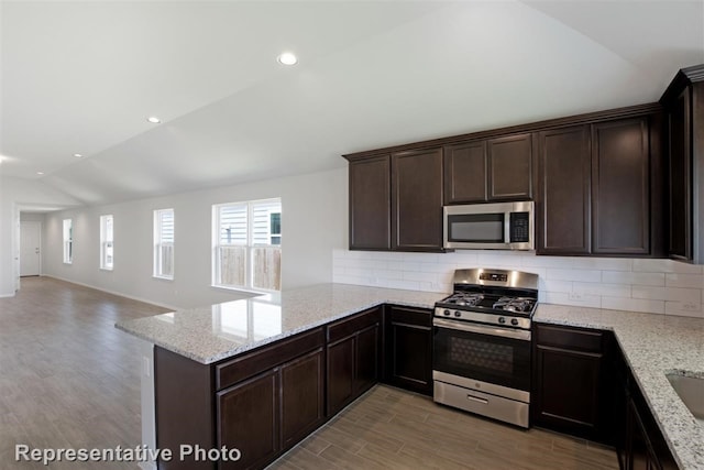 kitchen with appliances with stainless steel finishes, hardwood / wood-style flooring, lofted ceiling, and kitchen peninsula