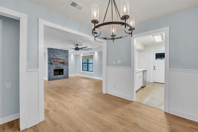 unfurnished dining area featuring brick wall, ceiling fan with notable chandelier, a fireplace, and light hardwood / wood-style flooring