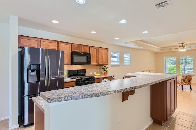 kitchen featuring light tile patterned flooring, a kitchen island, black appliances, backsplash, and ceiling fan