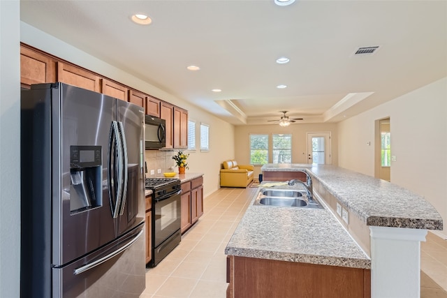 kitchen featuring a kitchen island with sink, sink, black appliances, a raised ceiling, and ceiling fan