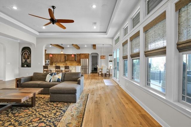 living room with a raised ceiling, ornamental molding, ceiling fan, and light hardwood / wood-style flooring