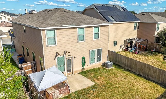 back of property with solar panels, a lawn, a patio, and central air condition unit