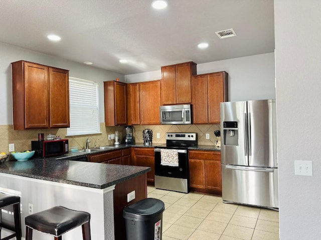 kitchen with visible vents, dark countertops, appliances with stainless steel finishes, a peninsula, and a sink