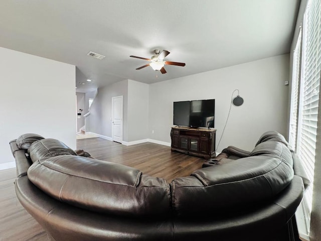 living room featuring ceiling fan, wood finished floors, visible vents, baseboards, and stairway