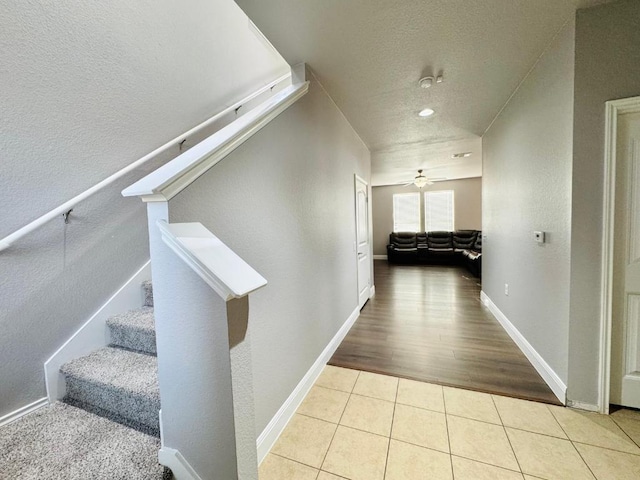 hallway featuring stairs, baseboards, a textured ceiling, and tile patterned floors