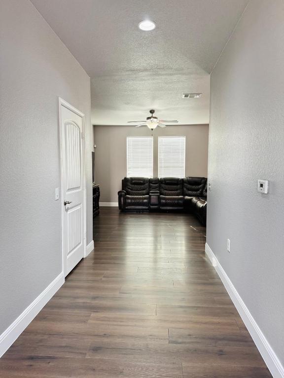 corridor with baseboards, a textured ceiling, visible vents, and wood finished floors