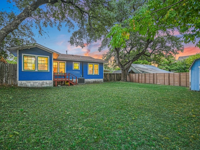 back house at dusk featuring a yard, a storage unit, and central AC