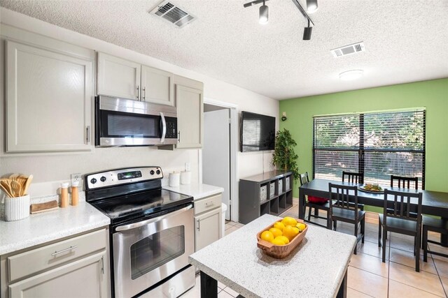 kitchen featuring track lighting, a textured ceiling, appliances with stainless steel finishes, and light tile patterned floors