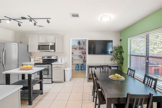 kitchen with light tile patterned floors, a textured ceiling, rail lighting, white cabinetry, and appliances with stainless steel finishes