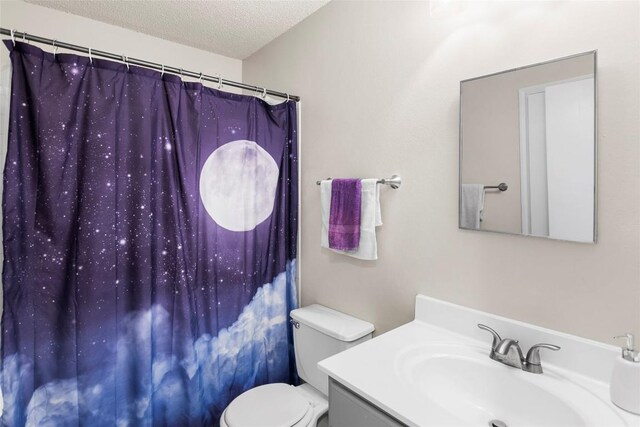 bathroom with a textured ceiling, curtained shower, vanity, and toilet