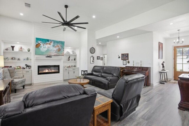 living room with ceiling fan with notable chandelier, a fireplace, light wood-type flooring, and built in features