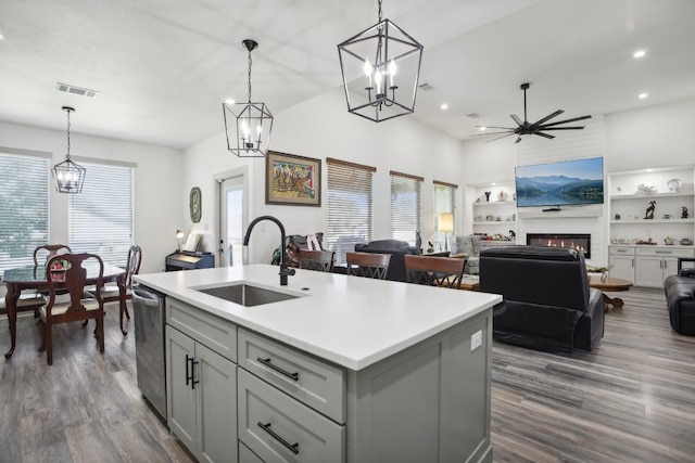 kitchen featuring hanging light fixtures, an island with sink, ceiling fan with notable chandelier, a fireplace, and sink