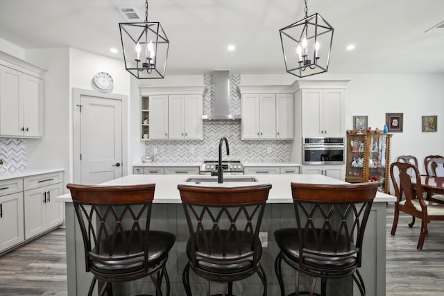 kitchen featuring a notable chandelier, wall chimney exhaust hood, stainless steel appliances, and an island with sink