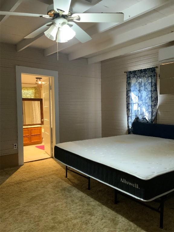 carpeted bedroom with ceiling fan, beamed ceiling, wooden walls, and connected bathroom