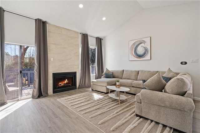 living room featuring vaulted ceiling, light hardwood / wood-style floors, and a tile fireplace