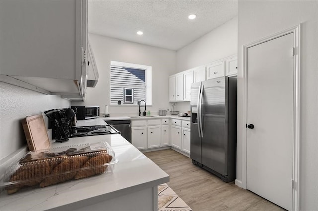 kitchen with white cabinets, sink, a textured ceiling, appliances with stainless steel finishes, and light wood-type flooring