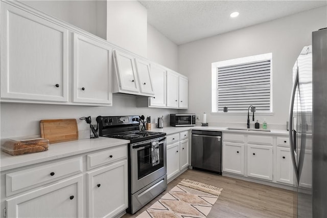 kitchen with stainless steel appliances, light wood-type flooring, sink, and white cabinetry