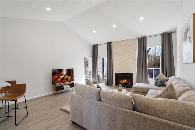 living room featuring a textured ceiling, light hardwood / wood-style flooring, a tiled fireplace, and vaulted ceiling