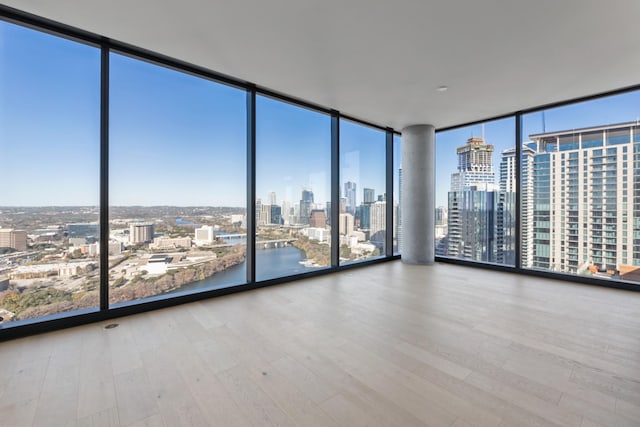 unfurnished room featuring floor to ceiling windows, a water view, and hardwood / wood-style flooring