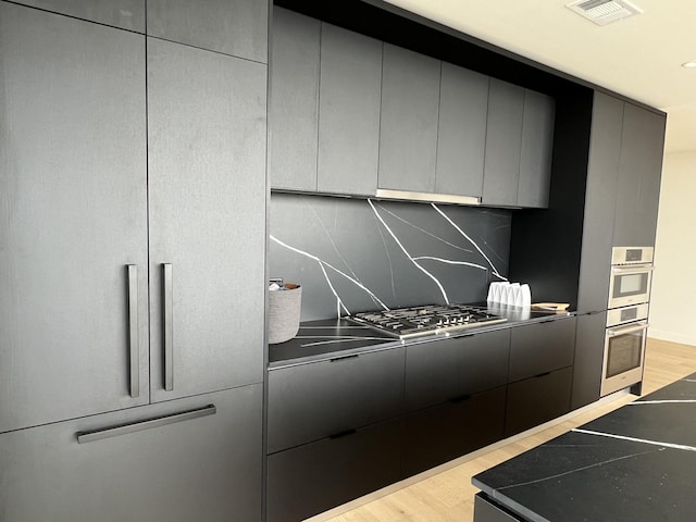 kitchen featuring light wood-type flooring, backsplash, stainless steel appliances, and gray cabinetry