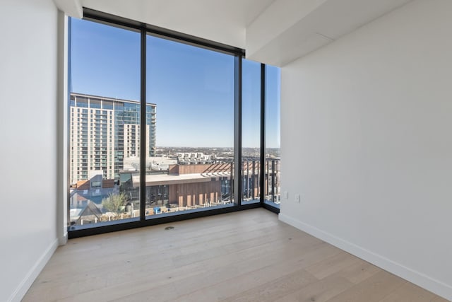 unfurnished room with floor to ceiling windows, a healthy amount of sunlight, and light hardwood / wood-style flooring