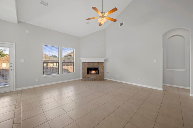 unfurnished living room with ceiling fan, a brick fireplace, light tile patterned floors, and high vaulted ceiling