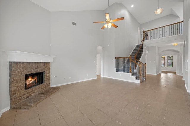 unfurnished living room with light tile patterned floors, ceiling fan, a brick fireplace, and high vaulted ceiling