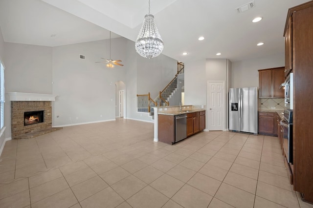 kitchen with appliances with stainless steel finishes, light stone counters, a brick fireplace, ceiling fan with notable chandelier, and sink