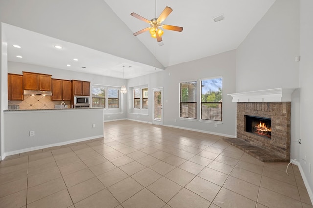 unfurnished living room featuring high vaulted ceiling, a brick fireplace, ceiling fan, and light tile patterned floors