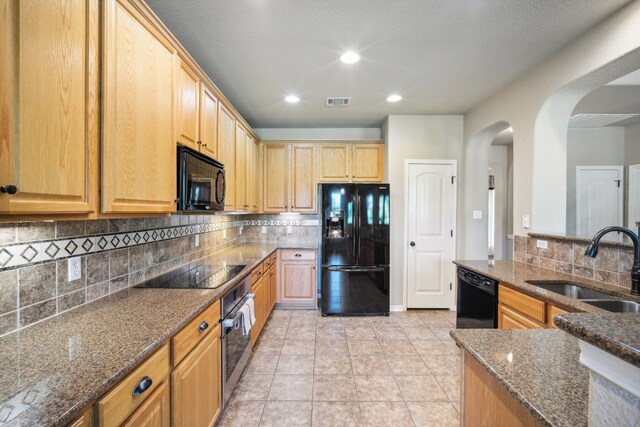 kitchen featuring black appliances, decorative backsplash, dark stone counters, and sink