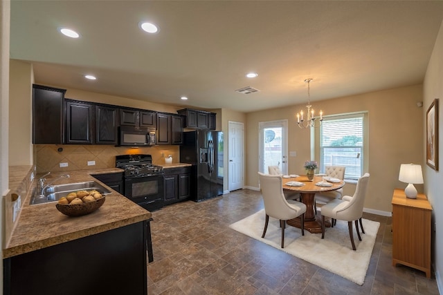 kitchen with an inviting chandelier, hanging light fixtures, black appliances, sink, and tasteful backsplash