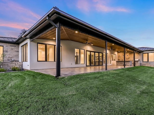 back house at dusk featuring a yard, ceiling fan, and a patio