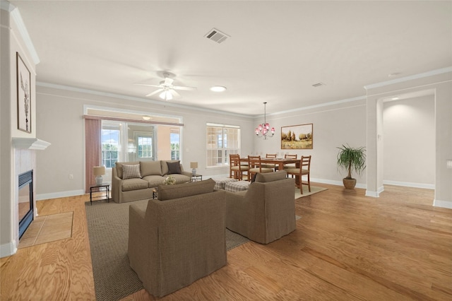 living room with light hardwood / wood-style flooring, ceiling fan, crown molding, and a tiled fireplace