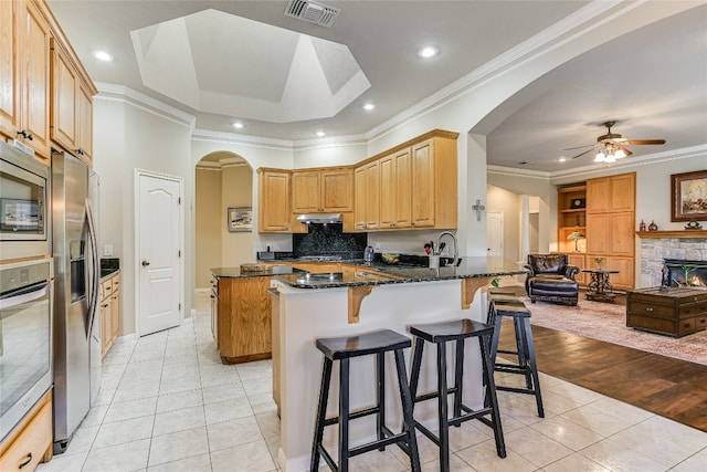 kitchen featuring kitchen peninsula, stainless steel appliances, ornamental molding, dark stone counters, and light tile patterned flooring