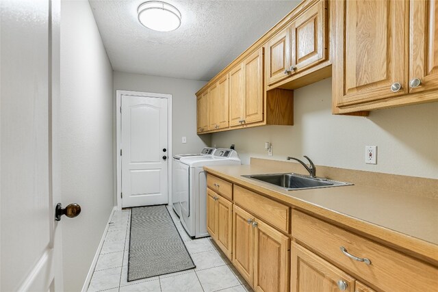 washroom with washing machine and dryer, light tile patterned flooring, a textured ceiling, cabinets, and sink