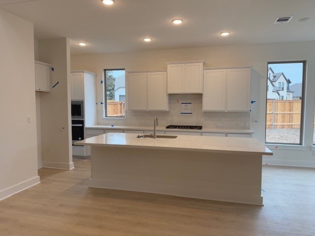 kitchen with white cabinetry, sink, a kitchen island with sink, black gas stovetop, and a healthy amount of sunlight