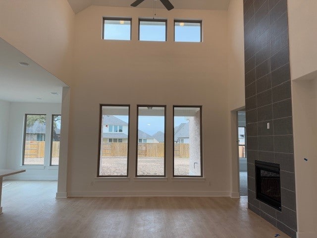 unfurnished living room with ceiling fan, a towering ceiling, light hardwood / wood-style floors, and a tile fireplace